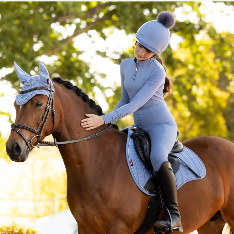 Rider in blue sits on brown horse with LeMieux Suede General Purpose Square in Powder Blue.