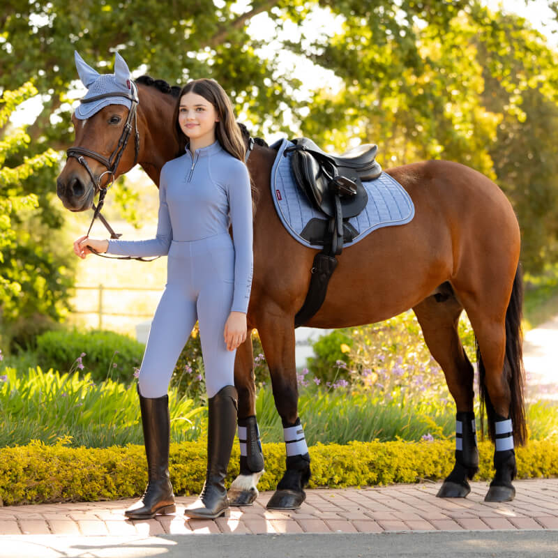 Young woman in light blue with horse, LeMieux Suede GP Square Powder Blue saddle pad.