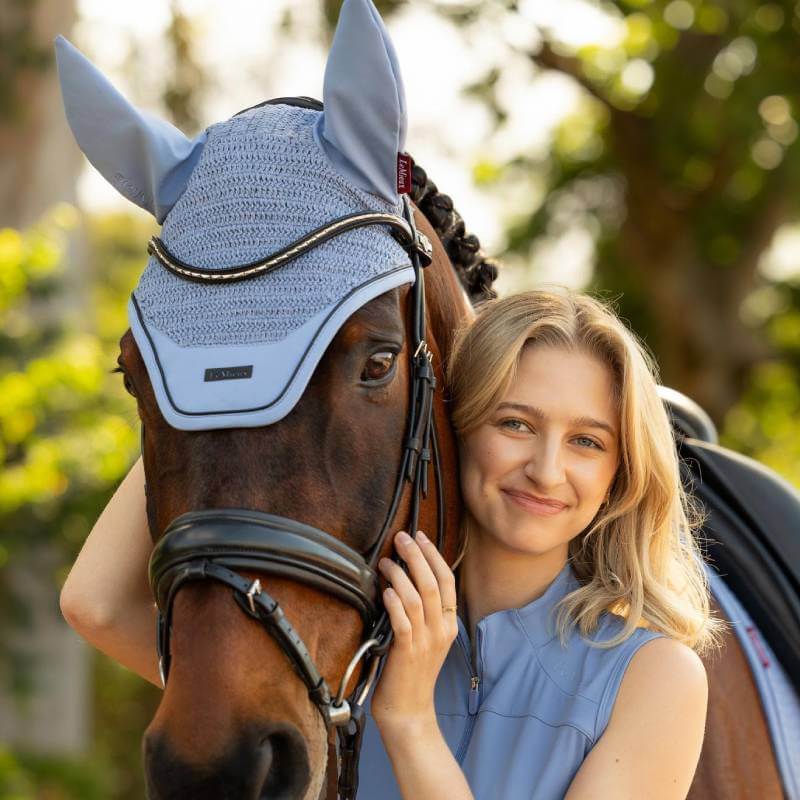 Woman hugs horse in LeMieux Essence Fly Hood Powder Blue outdoors.