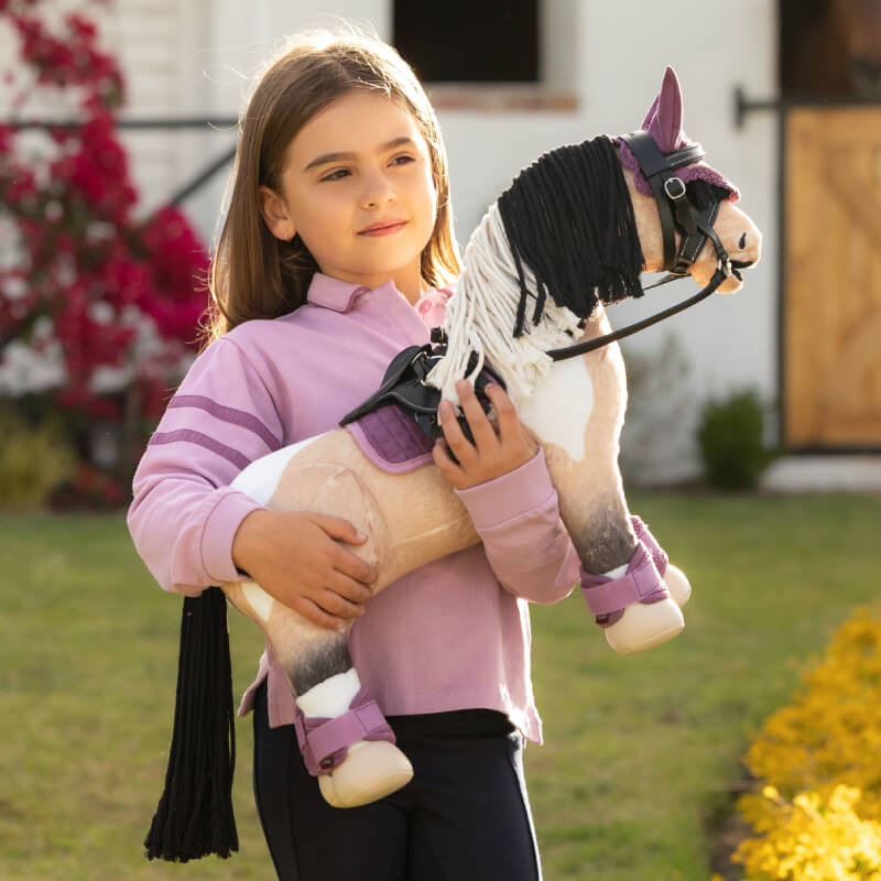Girl in a pink shirt holding LeMieux Toy Pony Toby outside in a garden.