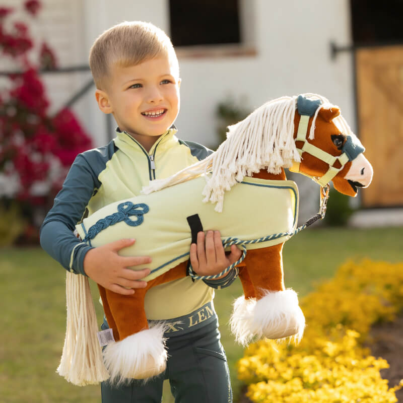 Smiling boy holds LeMieux Toy Pony Sundance with a plaitable mane outdoors on a sunny day.