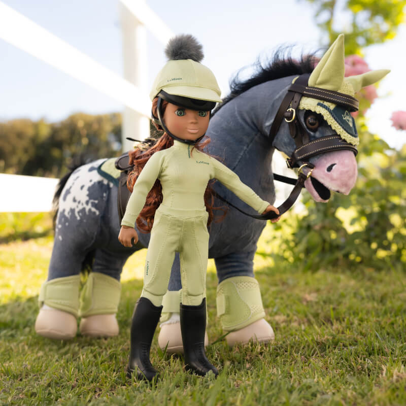 LeMieux Toy Rider Outfit Macaron doll poses with a horse on grass, white fence in background.