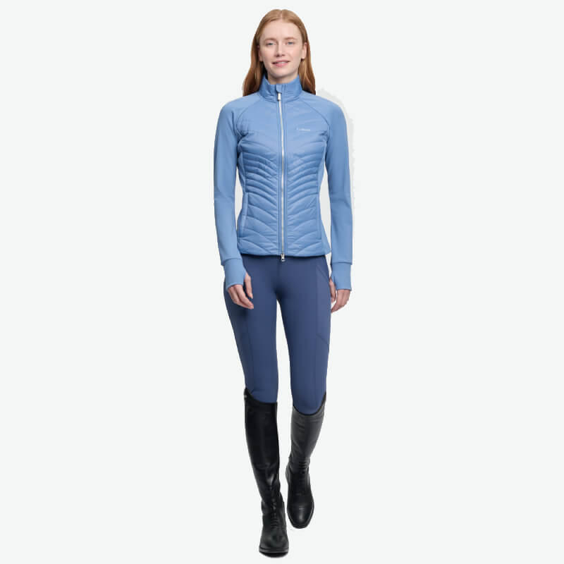 Smiling woman in a LeMieux Juliette Jacket Powder Blue, blue pants, and black knee-high boots.