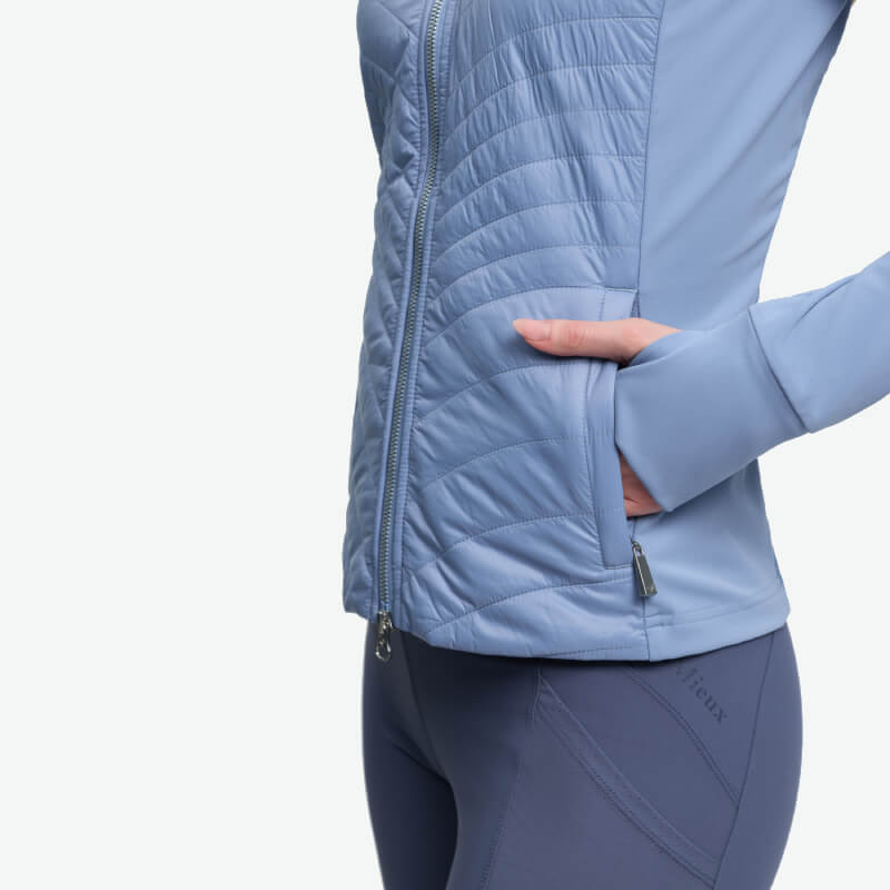 Person in fitted LeMieux Juliette Jacket Powder Blue and leggings, hand in pocket, side view.