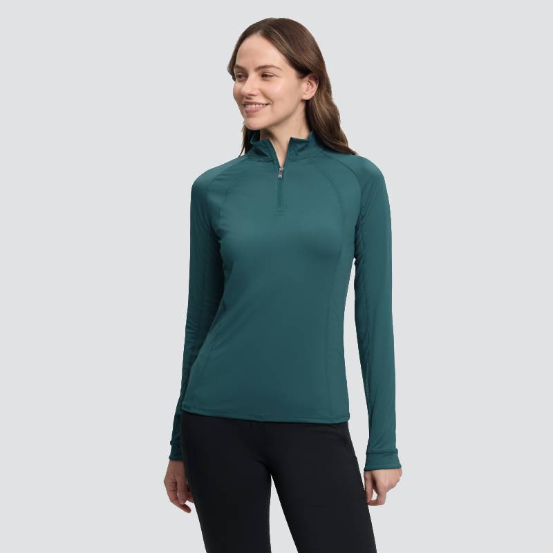 Woman in LeMieux Halle Lightweight Base Layer Jungle, teal, with black pants, on gray background.