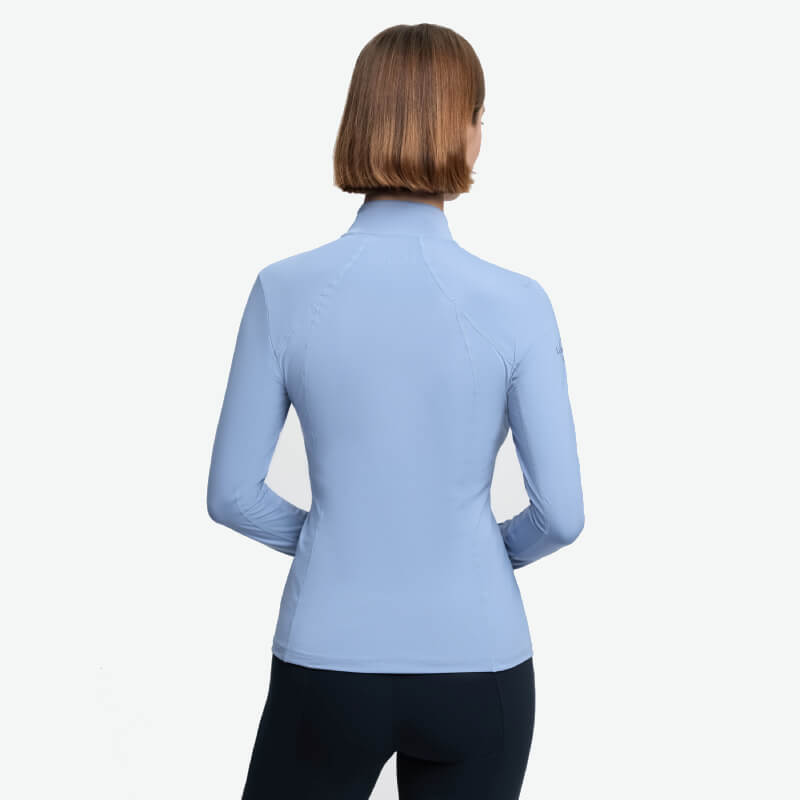 Woman with short hair wears a LeMieux Classique Baselayer Powder Blue, shown from the back.