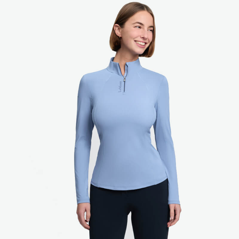 Woman in LeMieux Classique Baselayer Powder Blue, smiling, with dark pants and technical shirt.