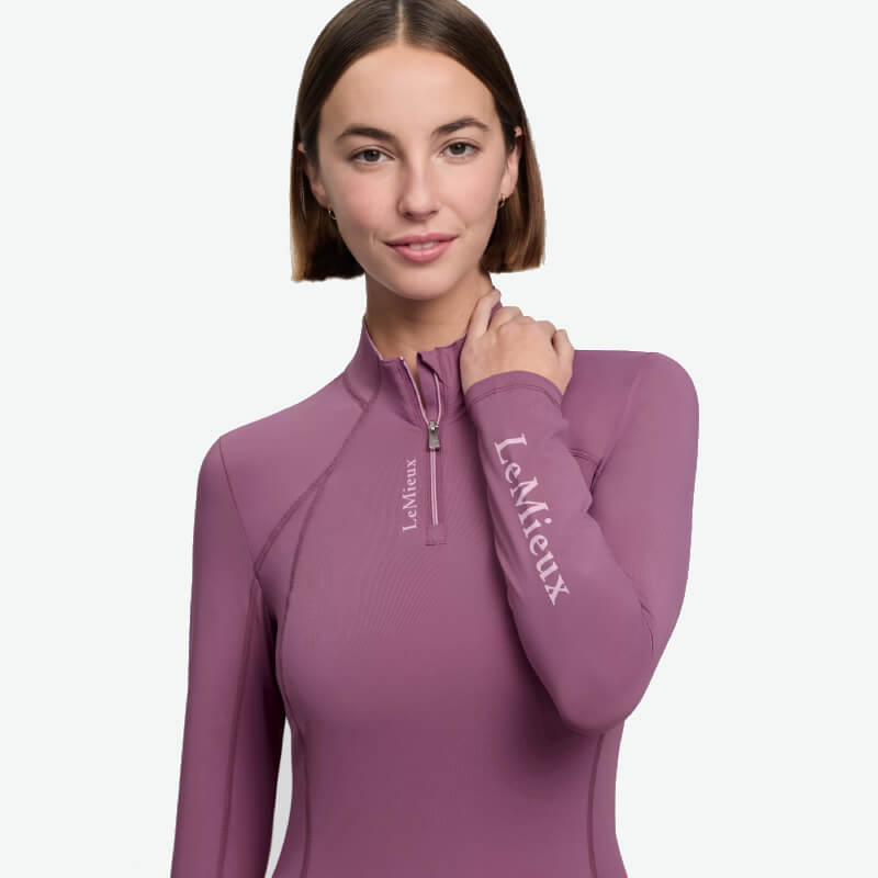 Woman smiles in a LeMieux Classique Baselayer Mallow, featuring LeMieux logo, facing camera.