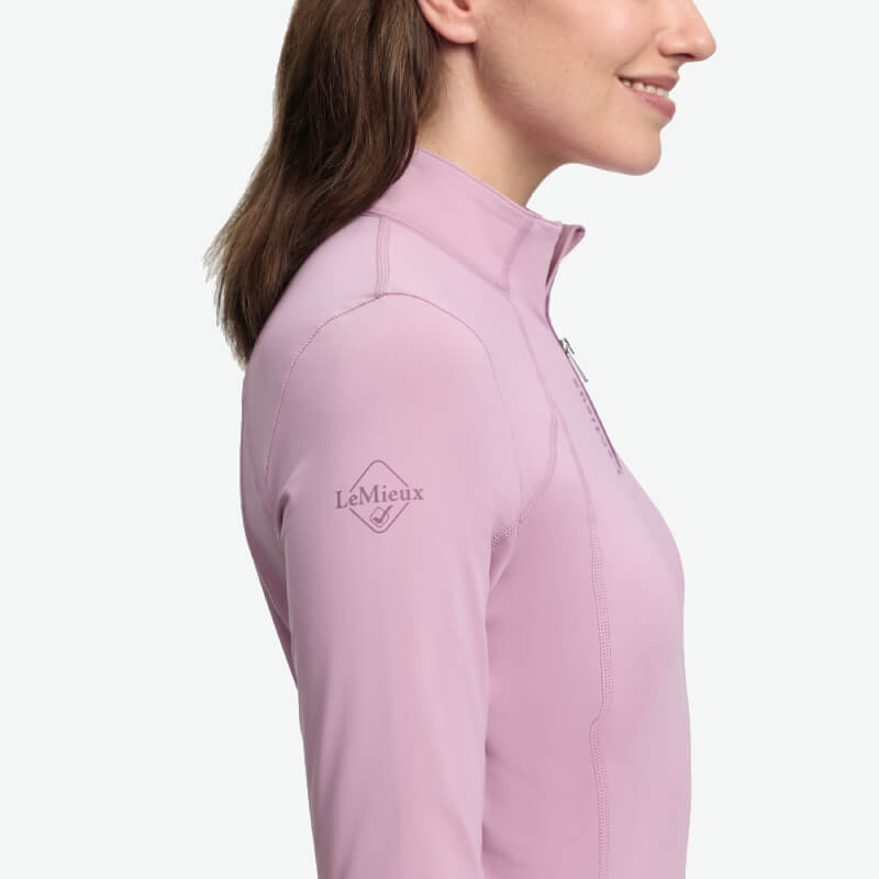 Woman in a LeMieux Classique Baselayer Fondant, light purple, logo on sleeve, facing right.