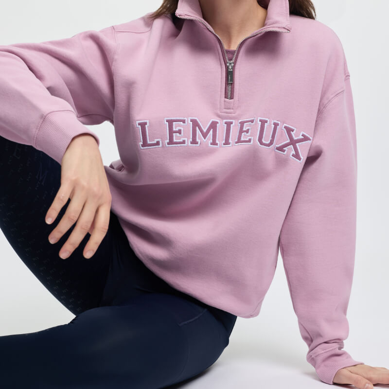 Smiling woman in pink LeMieux Kelsie Quarter Neck Sweat Fondant and dark pants, white background.