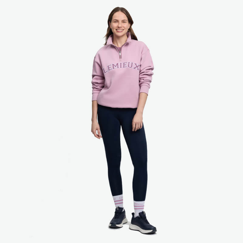 Woman in LeMieux Kelsie Quarter Neck Sweat Fondant, navy leggings, sneakers, on white backdrop.
