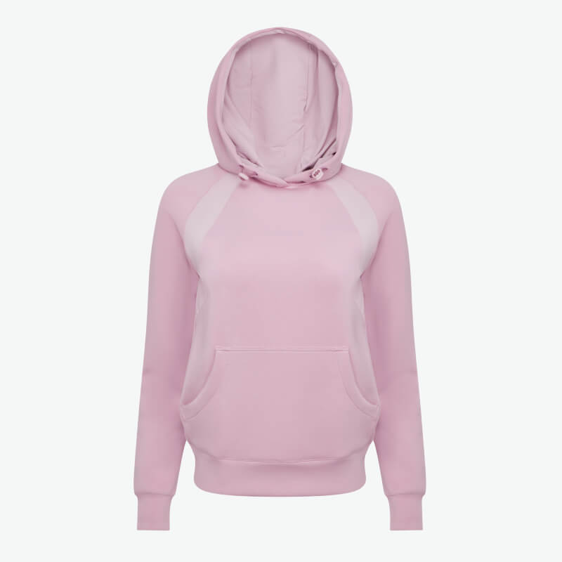 Woman in a LeMieux Nadine Airflow Hoodie Fondant and dark pants smiles against a plain backdrop.
