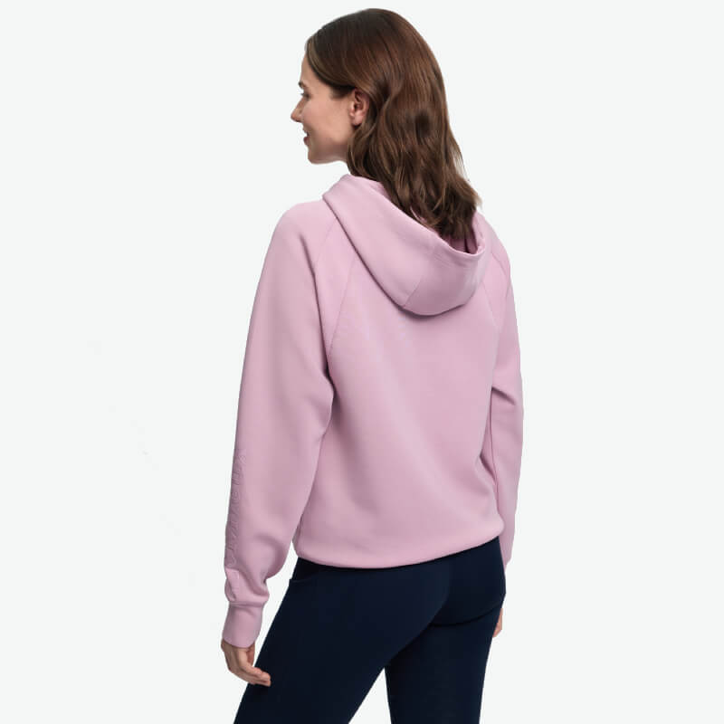 Woman in a LeMieux Nadine Airflow Hoodie Fondant and black pants, back view, white background.
