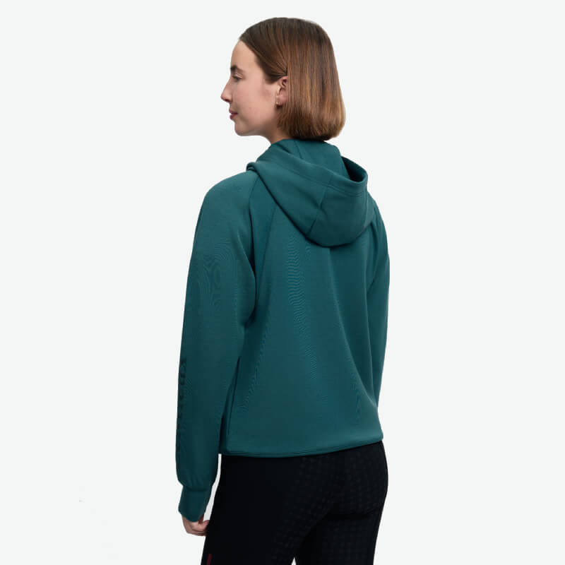 Person in green LeMieux Nadine Airflow Hoodie Jungle, back view, short brown hair, plain background.