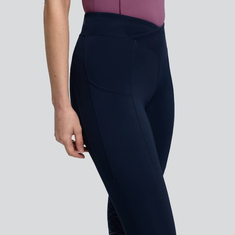 Model in LeMieux Simone Cross Over Half Seat Pull On Navy leggings, side view on gray background.