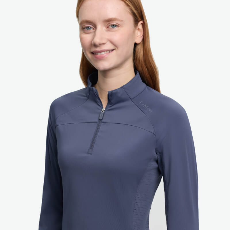 Smiling woman wears LeMieux Airflow Long Sleeve Baselayer Shadow, a moisture-wicking top.