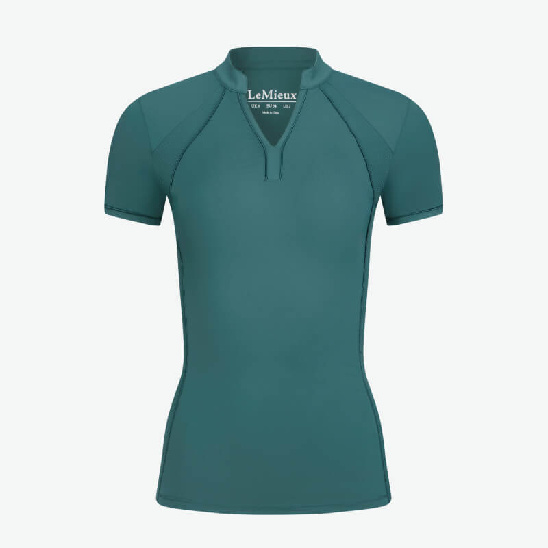 Woman in a LeMieux Lisa Mesh Baselayer Jungle and black pants stands against a plain background.