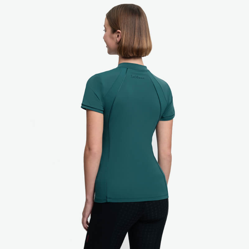 Woman wears LeMieux Lisa Mesh Baselayer Jungle, back to camera, against white background.