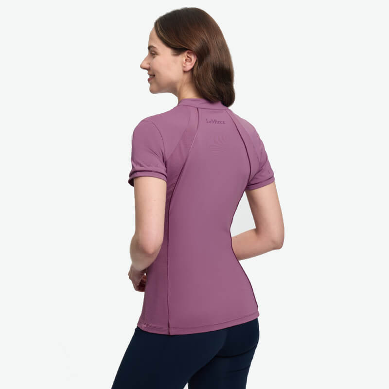 Woman in a LeMieux Lisa Mesh Baselayer Mallow and black pants, standing with back to camera.