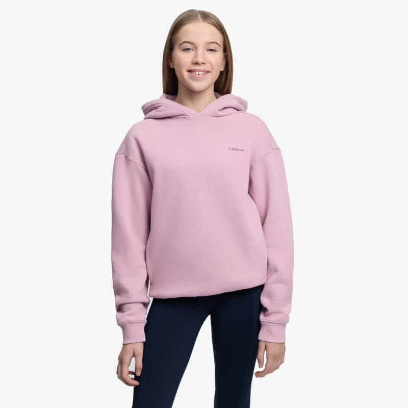 Teen girl smiles in LeMieux Young Rider Sia Hoodie Fondant, wearing dark pants, on white background.