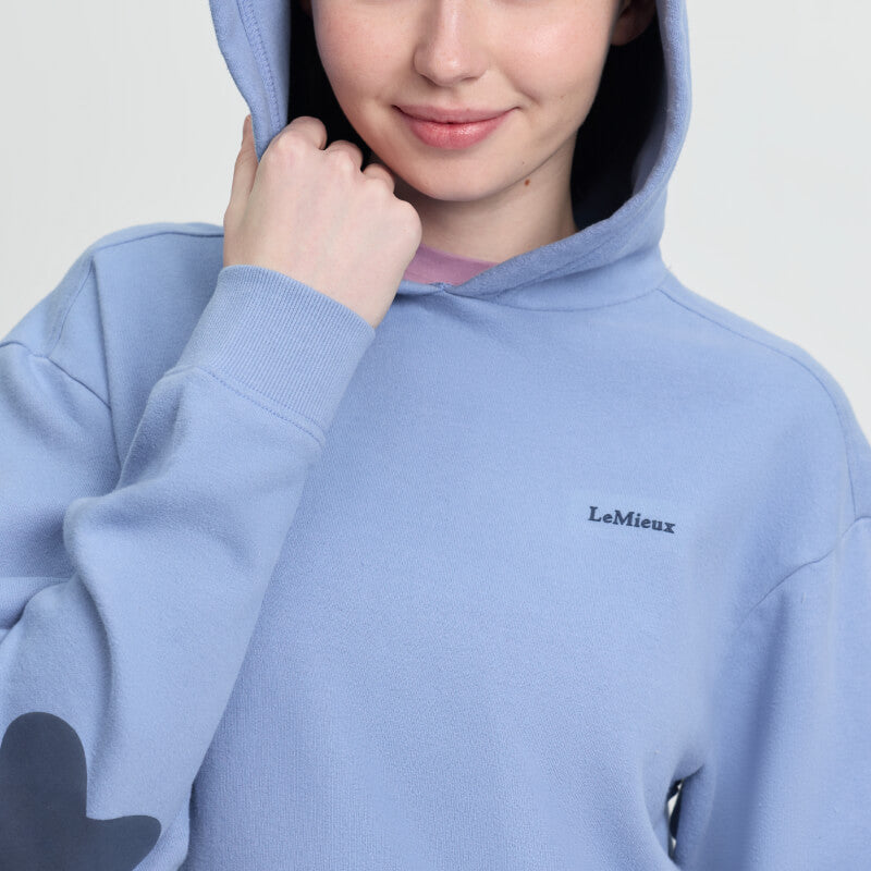 Smiling person wears LeMieux Young Rider Sia Hoodie Powder Blue, pulls hood over their head.