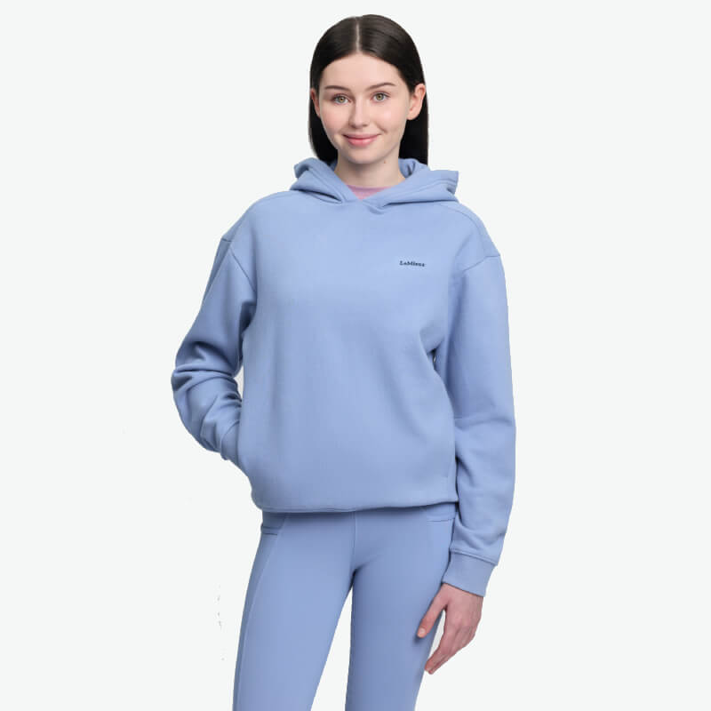 Smiling woman in LeMieux Young Rider Sia Hoodie Powder Blue, white background.