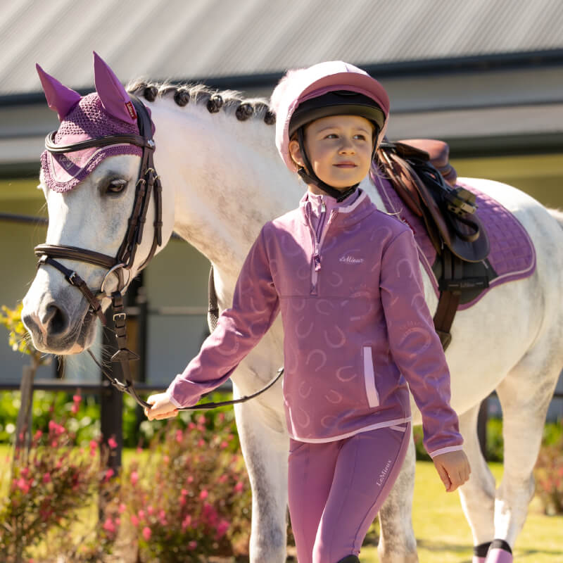 Child in LeMieux Mini Maggie Fleece Mallow leads white horse with matching purple accessories.