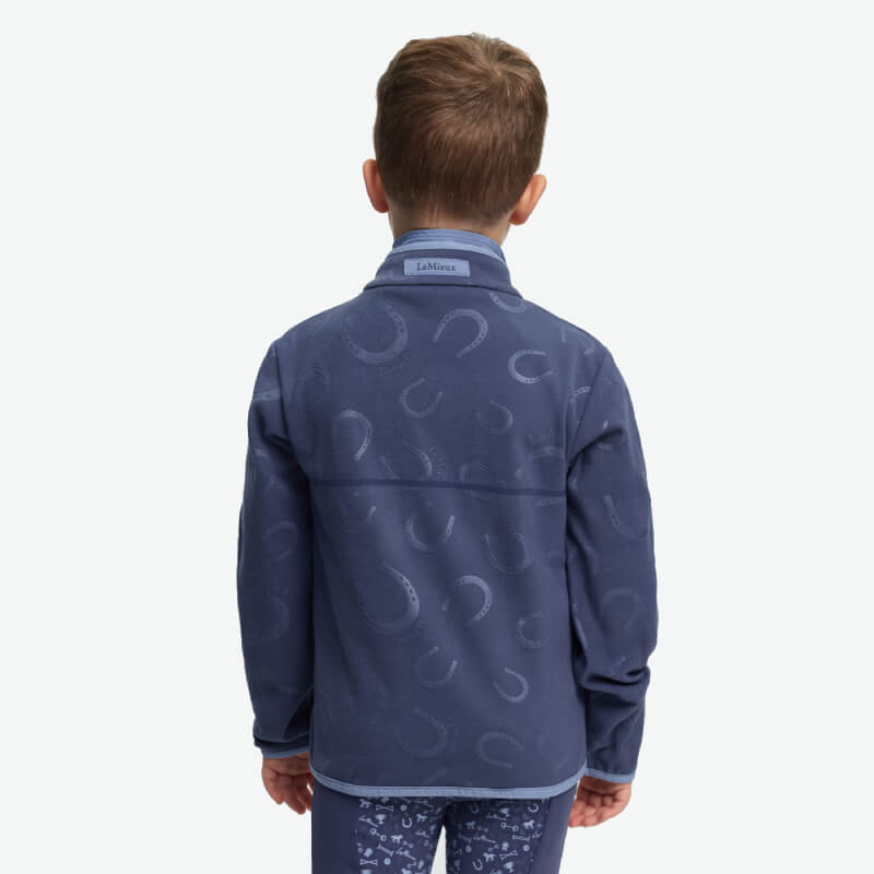 Smiling boy in LeMieux Mini Maggie Fleece Shadow with horseshoe pattern, on white background.