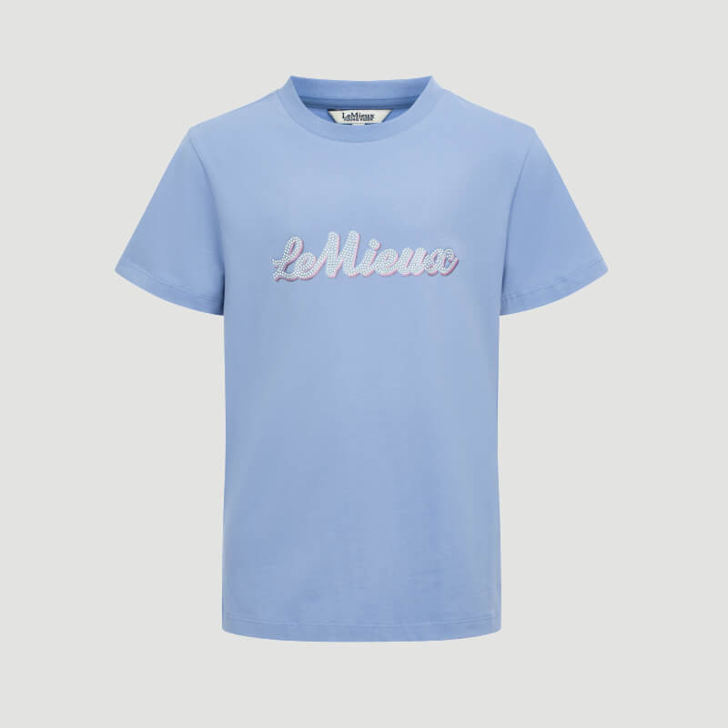 Teen girl in LeMieux Young Rider Arianna T-Shirt Powder Blue and pink pants, smiling at camera.