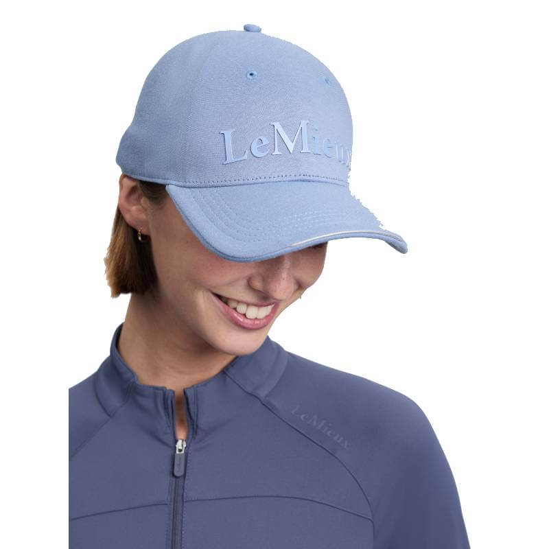 Woman in LeMieux Lara Cap Powder Blue, smiling and looking down, wearing a matching jacket.