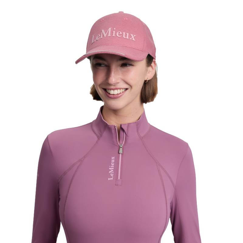 Smiling woman in a LeMieux Lara Cap in Mallow and matching top, both with LeMieux logos.