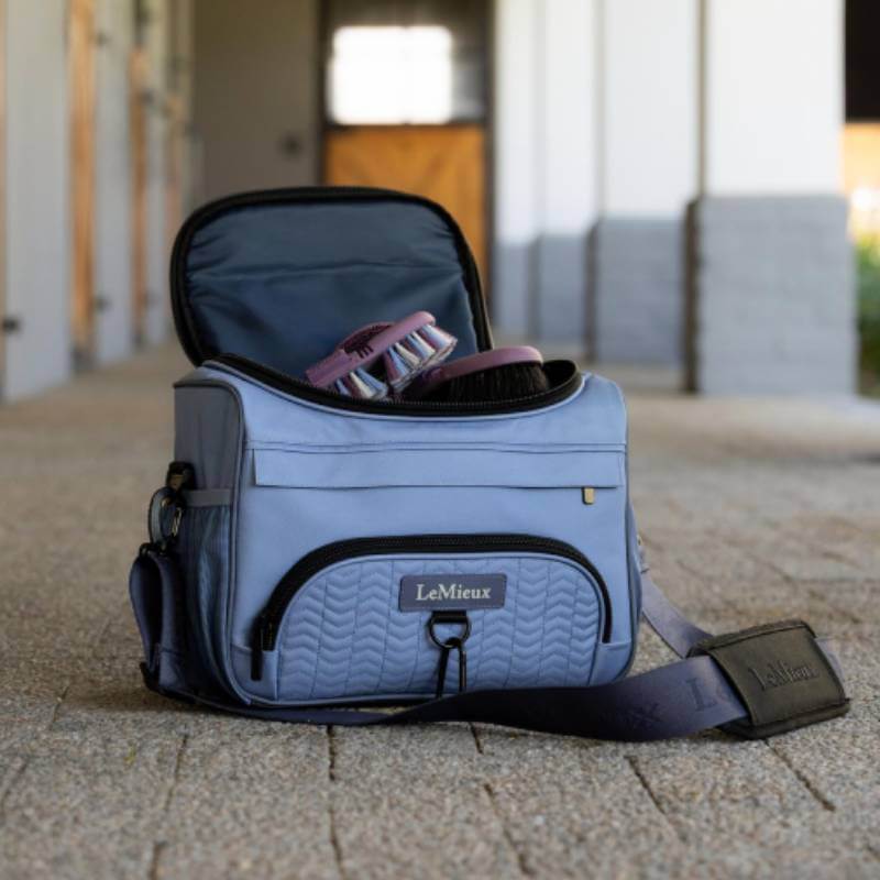 A LeMieux ProKit Lite Powder Blue bag (One Size) with brushes sits on a stone floor, strap forward.
