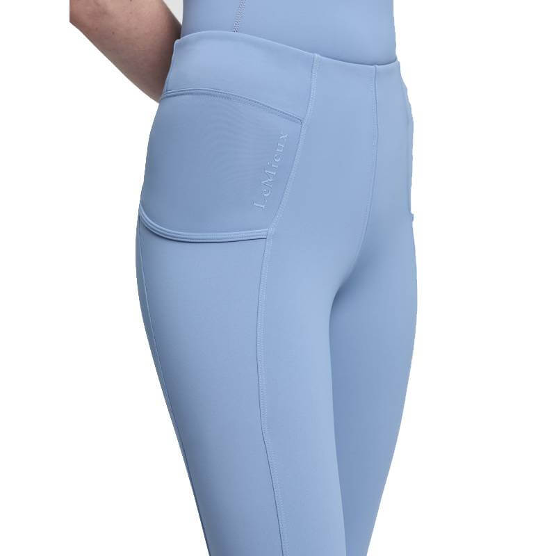 Woman wears LeMieux Young Rider Orla Pull On Breech in Powder Blue with side pocket and logo.