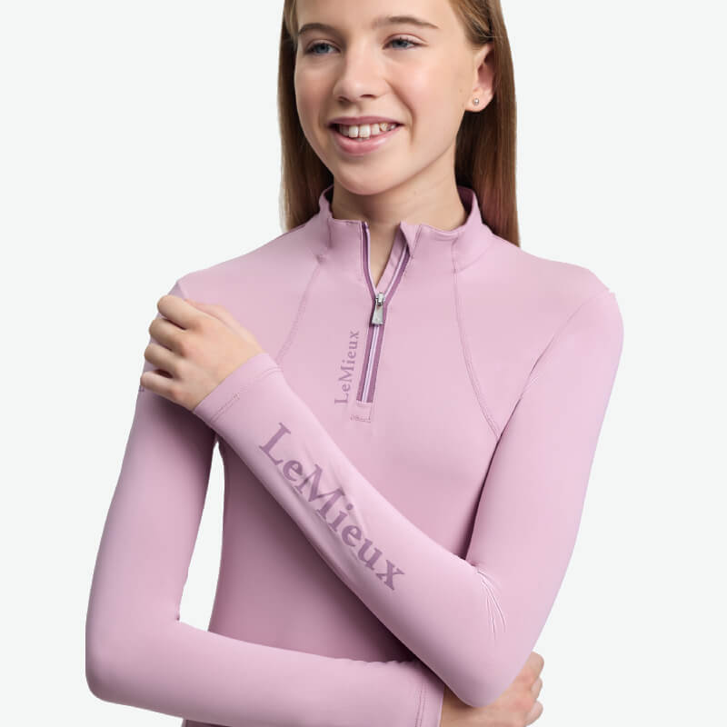 Smiling girl in a LeMieux Young Rider Classique Baselayer Fondant, arms crossed.