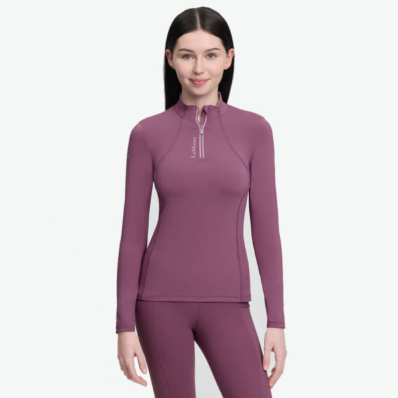 Woman in a LeMieux Young Rider Classique Baselayer Mallow, standing and smiling at camera.