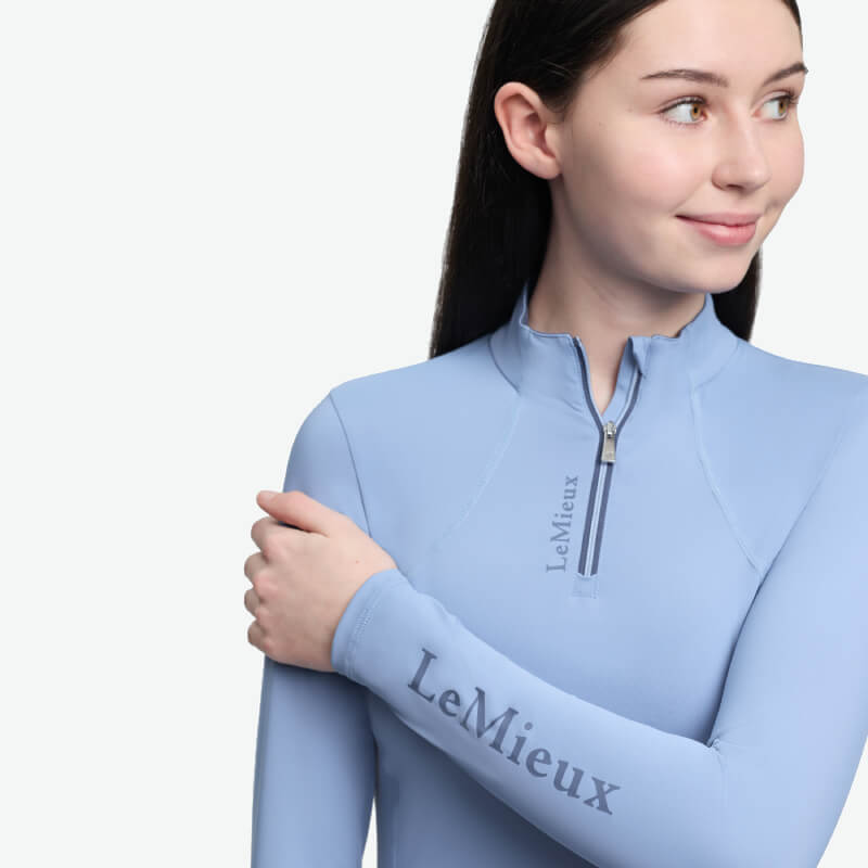 Smiling woman in LeMieux Young Rider Classique Baselayer Powder Blue, looking to the side.