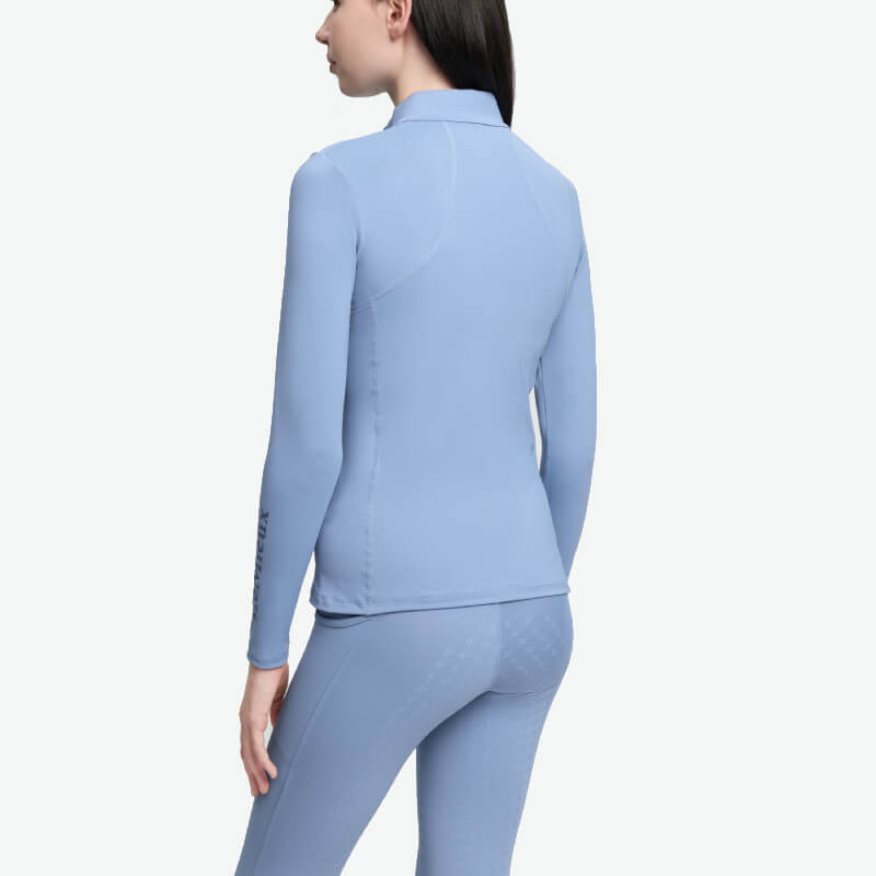 Woman in LeMieux Young Rider Classique Baselayer Powder Blue stands facing away.