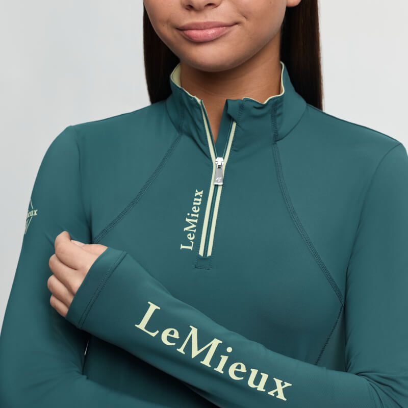 Woman in LeMieux Young Rider Classique Baselayer Jungle, logo on collar and sleeve, smiling.