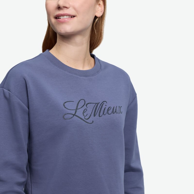 Woman in a LeMieux Christina Crew Sweat Shadow, blue with cursive logo and performance fabric.