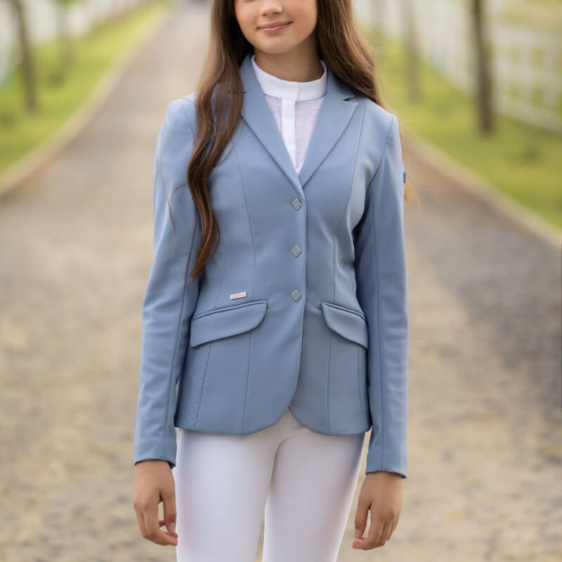 Woman wears LeMieux Young Rider Kennedy Show Jacket Powder Blue and white pants against white.