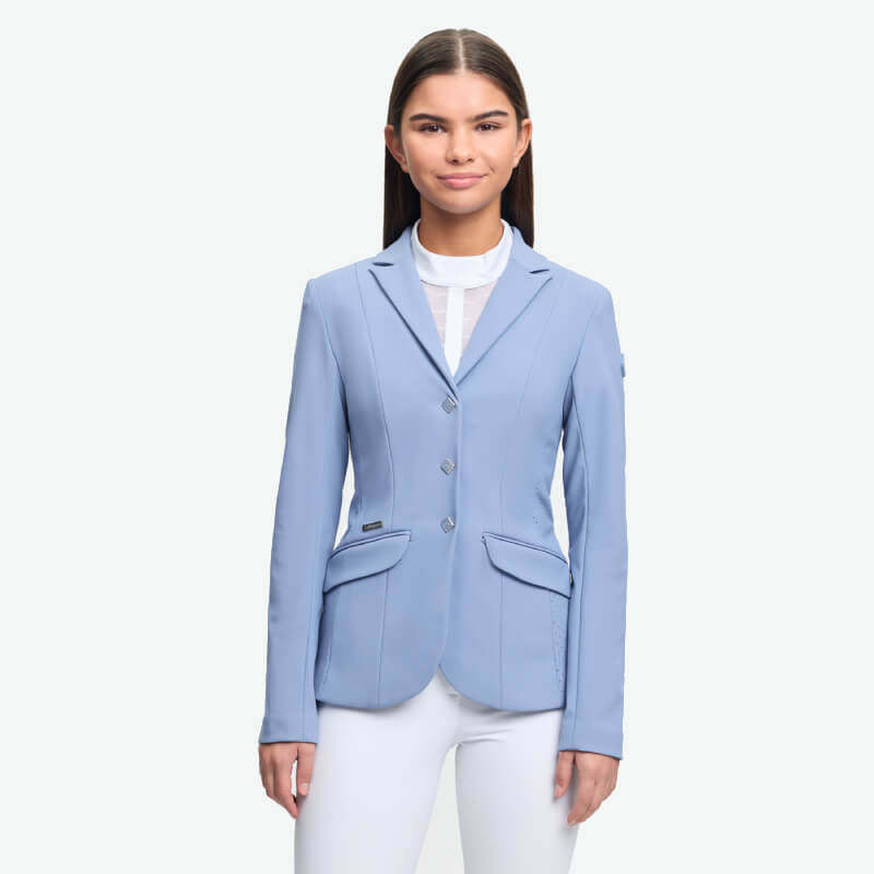Woman wears LeMieux Young Rider Kennedy Show Jacket Powder Blue and white pants against white.