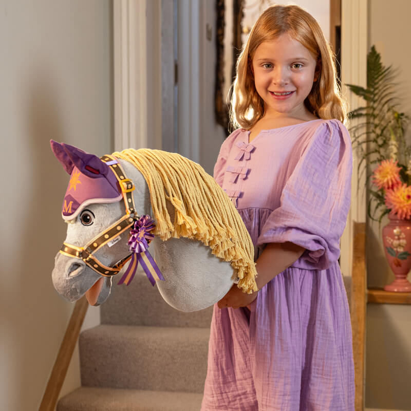 Girl in purple dress holds LeMieux Disney Hobby Horse Maximus on a staircase.