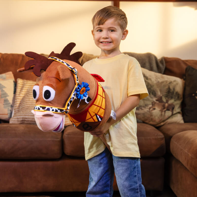 Smiling boy with LeMieux Disney Hobby Horse Bullseye, standing in front of a brown couch.