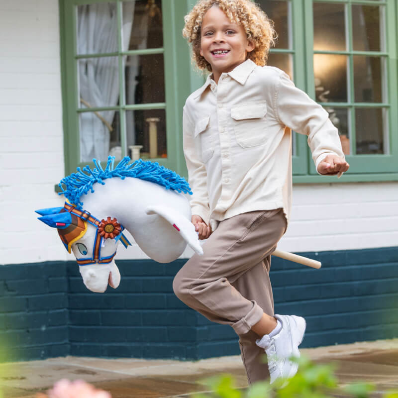 Happy child with LeMieux Disney Hobby Horse Accessories Set Pegasus by green-trimmed windows.