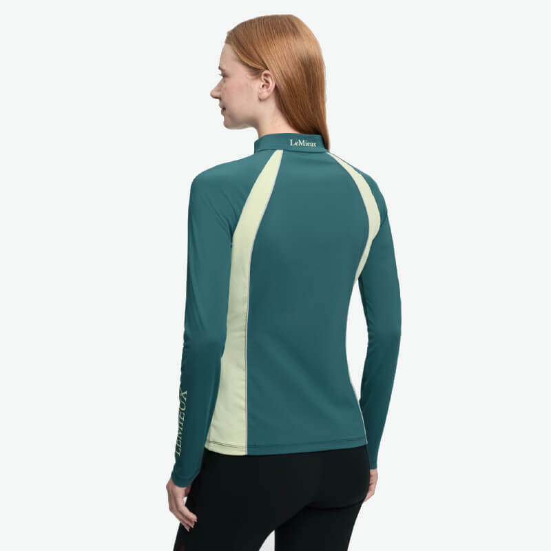Woman with long red hair wears a LeMieux Philippa Mesh Baselayer Jungle, facing away.
