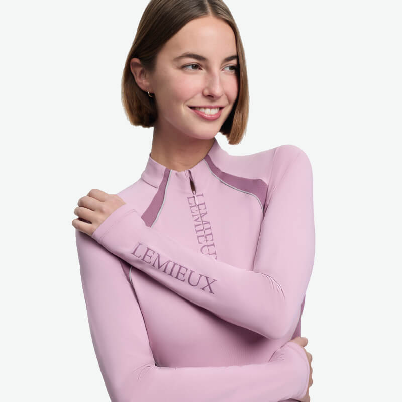 Woman in a LeMieux Philippa Mesh Baselayer Fondant and black leggings smiles at the camera.