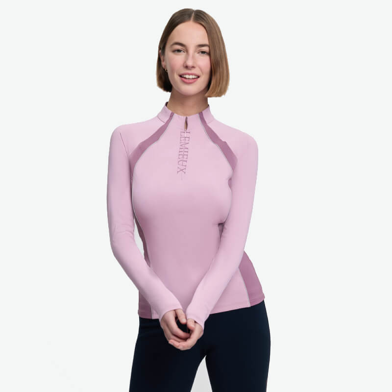 Woman in a LeMieux Philippa Mesh Baselayer Fondant and black leggings smiles at the camera.