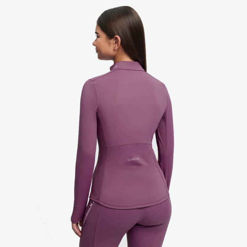 Girl in LeMieux Young Rider Airflow Baselayer Mallow smiles, facing forward, on white background.