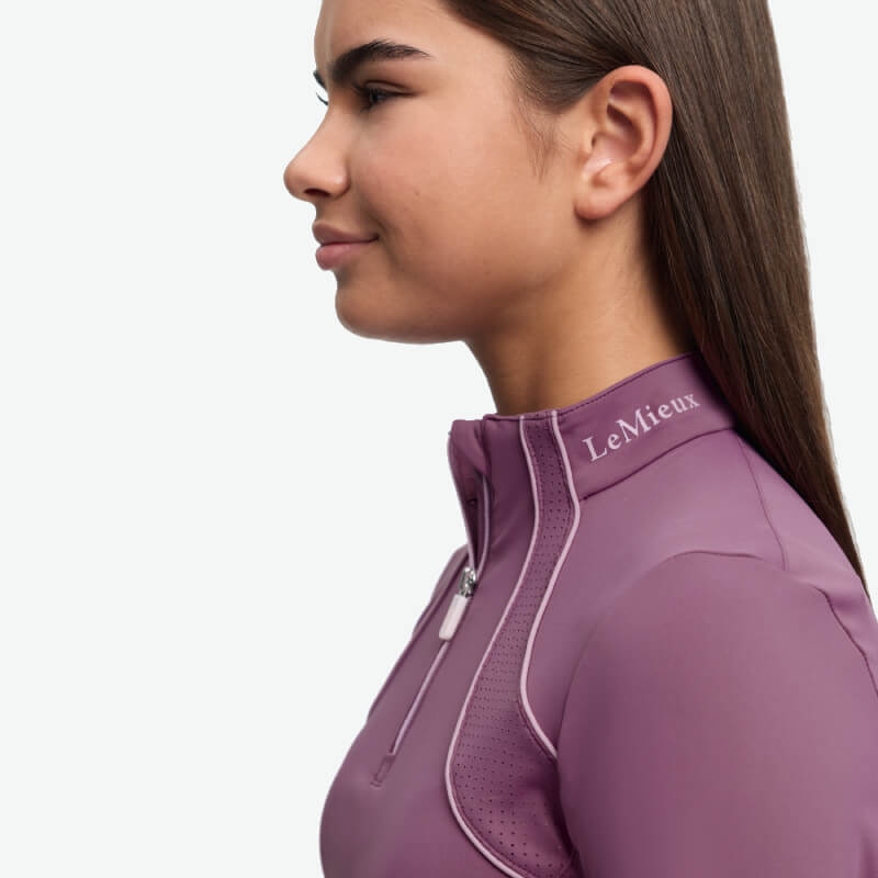 Girl in a purple LeMieux Young Rider Airflow Baselayer Mallow, facing left on white background.