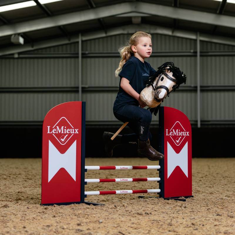 Young girl jumps over the LeMieux Hobby Horse Jump Chilli while riding indoors.